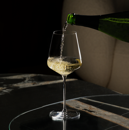 Lehmann Bacchus 55 waarin mousserende wijn uit een groene fles wordt geschonken, op een tafeltje van donker marmer voor een beige bank