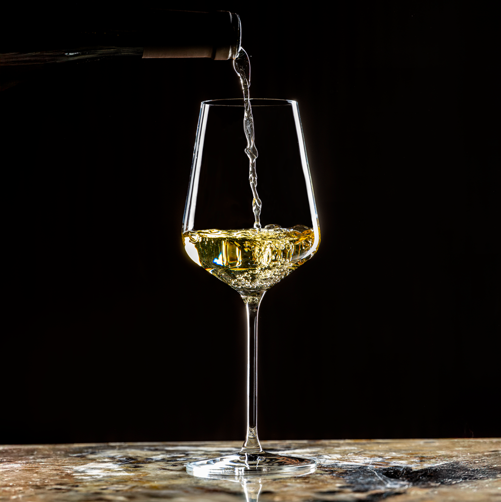 Lehmann Hera 39 waarin witte wijn uit een fles wordt geschonken, op een marmeren blad voor een zwarte achtergrond