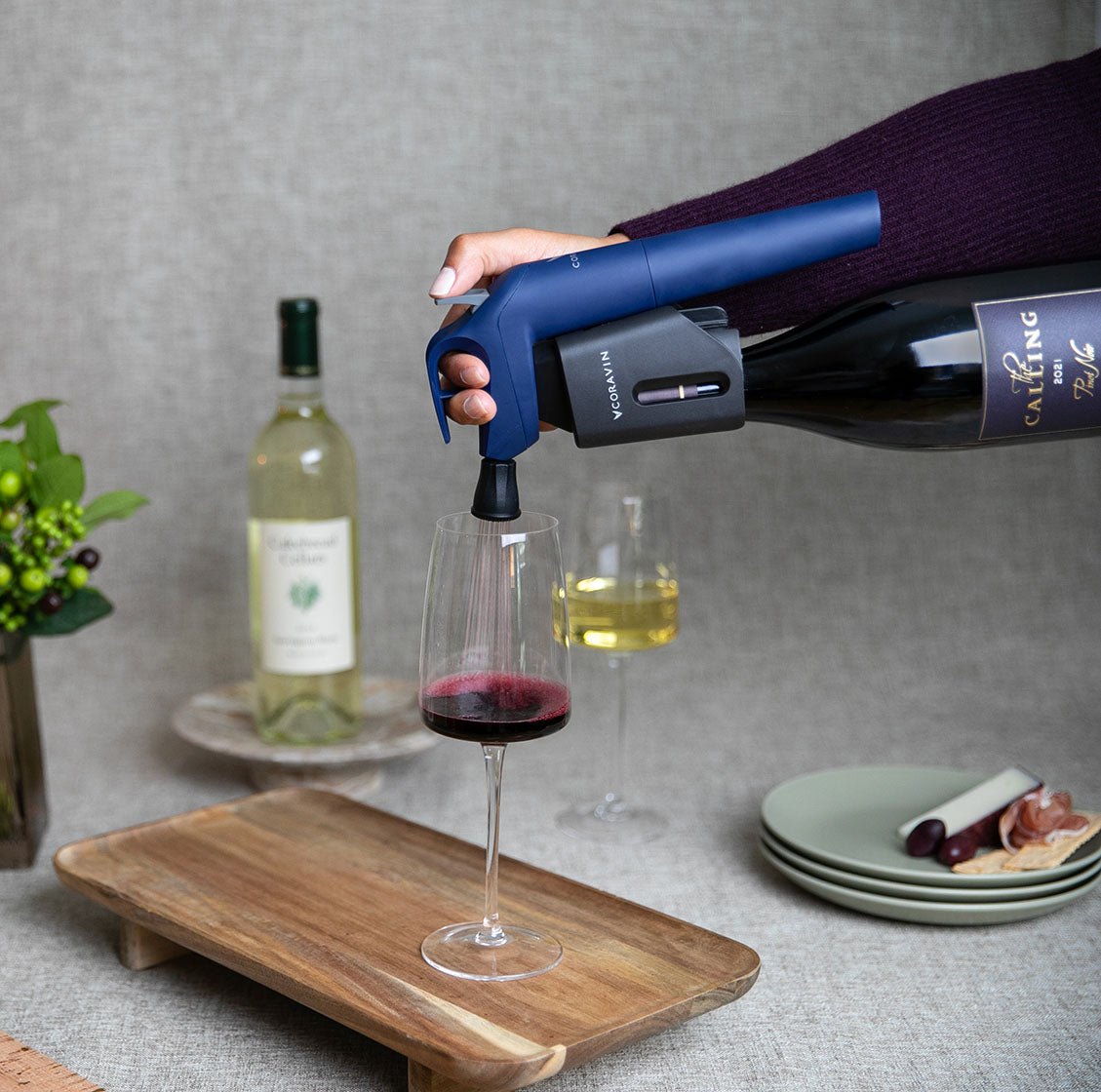 Een glas wijn wordt met een Coravin geschonken aan een gedekte tafel met witte en rode wijn