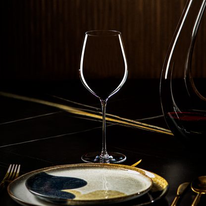 Leeg Lehmann Hommage-glas van 60 cl op een gedekte tafel met een keramisch bord en goudkleurig bestek, rechts een karaf met rode wijn