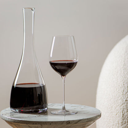 Lehmann Hommage-glas van 60 cl en een karaf, allebei met rode wijn, op een marmeren bijzettafel voor een lichte muur