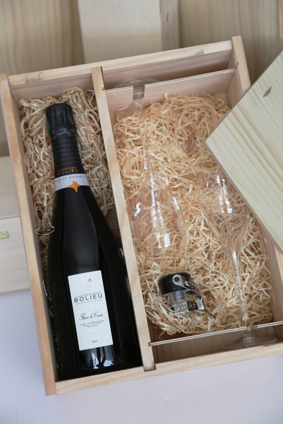 Houten kist met twee vakken: een fles, twee glazen en een stopper op houtwol.